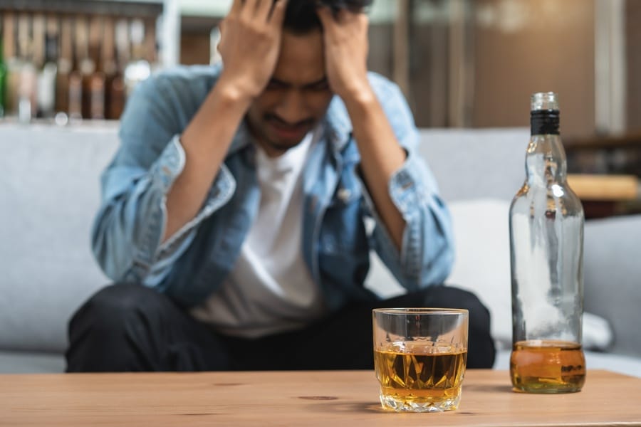 man holding head in distress with beer on table, showing alcohol effects in body